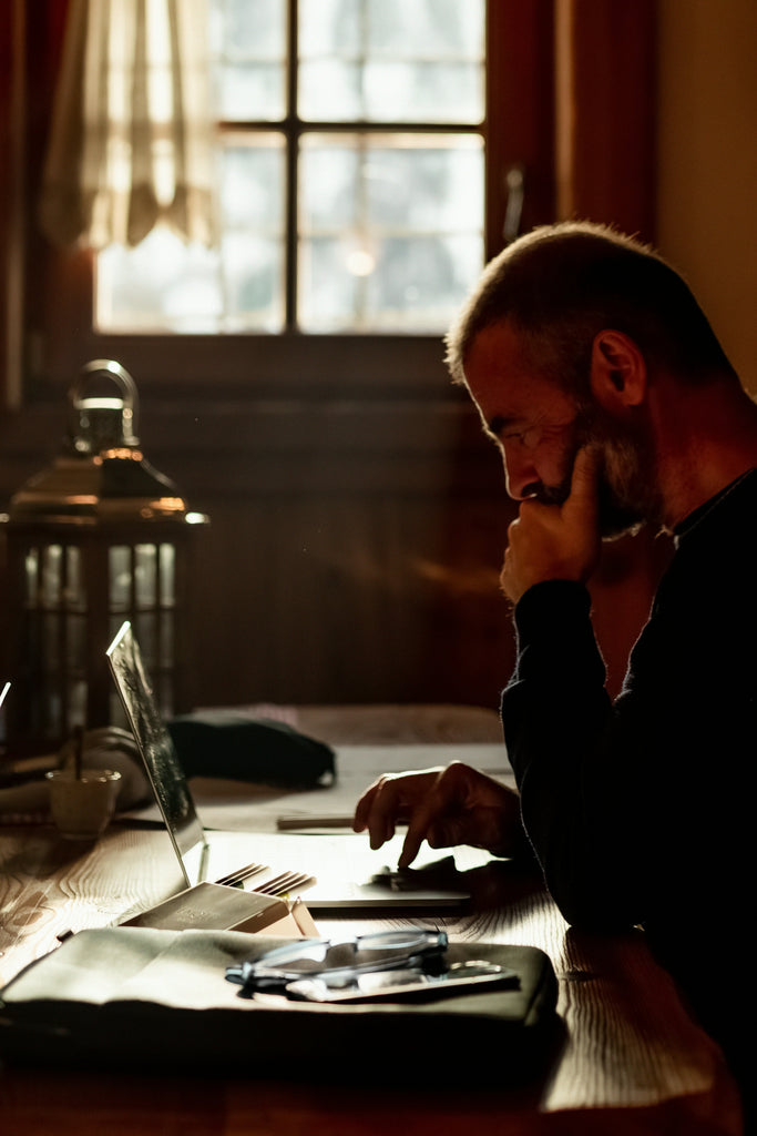 Man sitting a a desk with a window in the background, looking at his computer, working and focusing in natural light