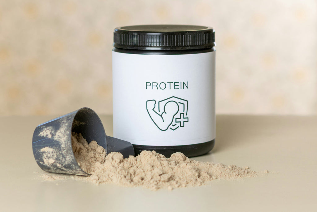 Protein canister sitting on a table with a scoop of protein powder spilled out on the table